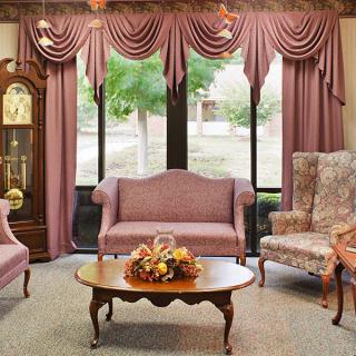 A classic style living room with elegant furniture and decor, featuring a grandfather clock and large windows with draped curtains.