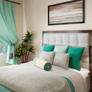 A modern bedroom with teal accents featuring a neatly made bed, decorative pillows, artwork, and a potted plant by the window.