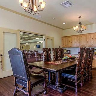 A traditional dining room with a large wooden table and ornate chairs, illuminated by chandeliers.