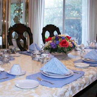 A formal dining table elegantly set with blue napkins, silver cutlery, and a vibrant floral centerpiece.