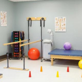 A physical therapy room equipped with balance bars, exercise balls, and various rehabilitation equipment.