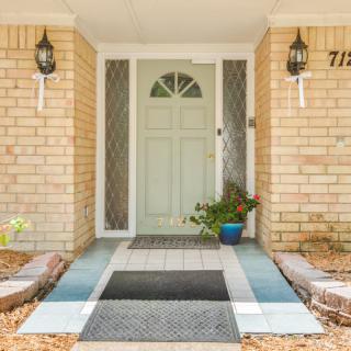 A welcoming front entrance with a light-colored door, flanked by brick walls and decorated with potted plants.