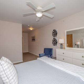 A modern bedroom with a bed, dresser, and a ceiling fan.