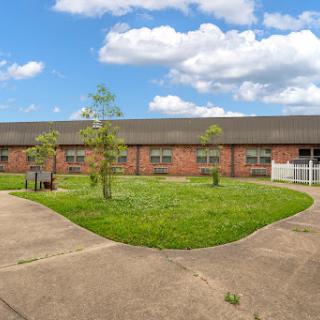 A well-maintained residential building surrounded by green grass and trees under a partly cloudy sky.