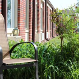 A tranquil outdoor seating area beside a brick building, surrounded by lush greenery.