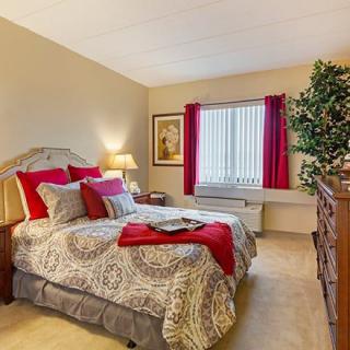 A cozy bedroom with elegant decor, featuring a comfortable bed adorned with red accents and warm lighting.