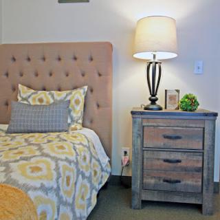 A cozy bedroom featuring a stylish tufted headboard, patterned bedding, a rustic nightstand with a lamp, and greenery for a touch of freshness.