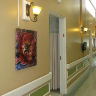 A hallway featuring a colorful painting on the wall next to a softly lit sconce and an open door.