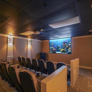 A cozy home theater setup with multiple rows of seating and a large projector screen displaying an underwater scene.