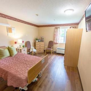 A cozy bedroom featuring a bed with colorful pillows, wooden flooring, and natural light coming through the window.