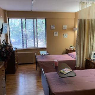 A serene hospital room featuring two beds, equipped with essential furniture and a view through the window.