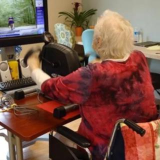 An elderly person using an indoor cycling device connected to a computer for exercise.