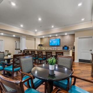 A modern dining area featuring elegant tables and chairs, with a television mounted on the wall and warm lighting illuminating the wooden floors.