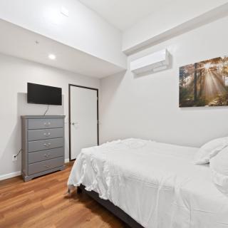 A minimalist bedroom featuring a bed, dresser, wall-mounted TV, and artwork.