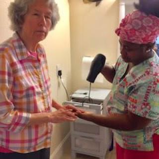 A caregiver assisting an elderly woman with hand care, using a handheld device.