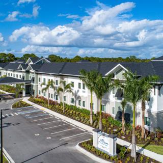 A modern apartment complex with palm trees and a spacious parking lot under a clear blue sky.