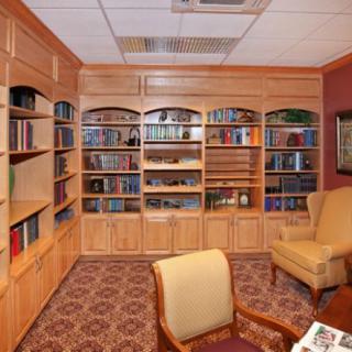 A cozy library corner with wooden bookshelves, comfortable chairs, and a patterned carpet.