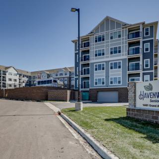 A modern apartment complex with multiple stories, featuring a sign at the entrance.