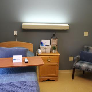 A cozy hospital room featuring a patient bed, a nightstand with medical supplies, and a comfortable chair.