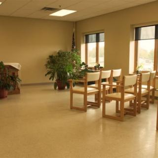 An empty room with wooden chairs, plants, and large windows letting in natural light.