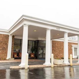 The entrance of a building with white columns and a brick exterior on an overcast day.