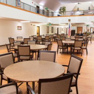 A spacious community dining area with multiple round tables and chairs, featuring an open ceiling design.