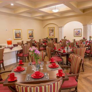A cozy dining room with elegantly set tables featuring red napkins and floral centerpieces.