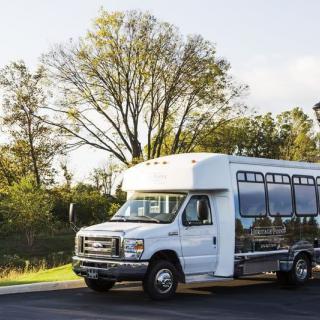 A small white shuttle bus parked on a sunny day with trees in the background.