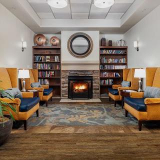A cozy library with armchairs and a fireplace, surrounded by bookshelves.