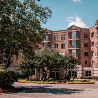 A brick apartment building with trees and landscaped surroundings on a sunny day.