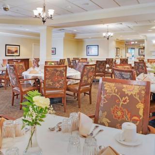An elegant dining room with neatly arranged tables and chairs, accented by floral decorations on the tables.