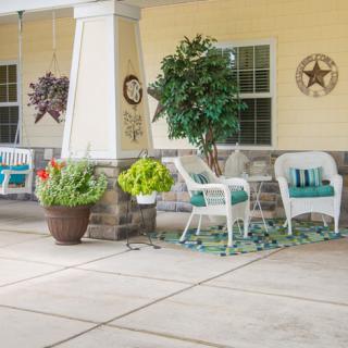 A cozy porch with white wicker chairs, a small table, and vibrant plants creating an inviting outdoor space.