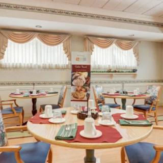 A neatly arranged dining room with several tables set for a meal, featuring elegant place settings and decorative curtains.