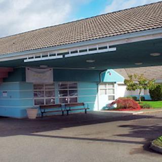 The image shows the entrance of a building with an awning and a bench outside.