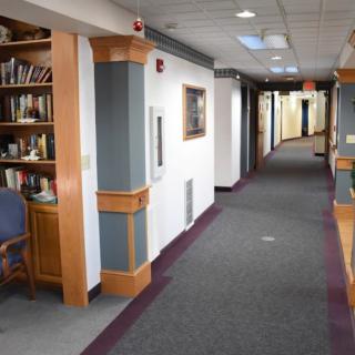 A quiet office hallway with carpeted floors and bookshelves lining the walls.