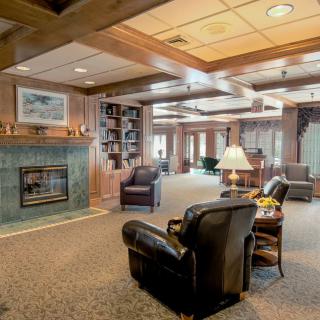 A cozy living room with wood paneling, featuring a fireplace, armchairs, and bookshelves.