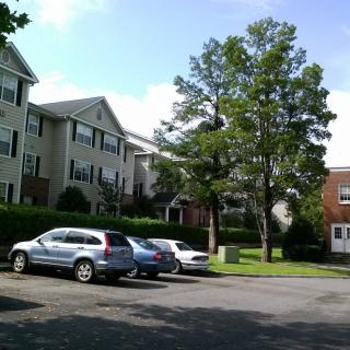 A residential apartment complex with parked cars and surrounding trees.