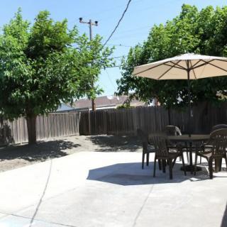 A sunny backyard patio with outdoor furniture and an umbrella, surrounded by trees.