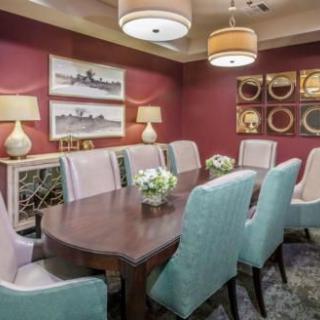 An elegant dining room with a long wooden table surrounded by upholstered chairs, adorned with wall art and soft lighting.