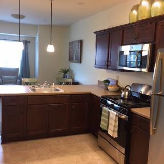 A modern kitchen with wooden cabinets, stainless steel appliances, and pendant lighting over the countertops.