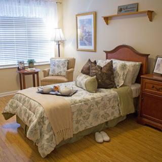 A cozy bedroom with a neatly made bed, complete with decorative pillows and a soft blanket. A chair sits beside the window, providing a comfortable reading spot.