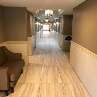 A long, well-lit hallway with tile flooring and a chair placed near the wall.