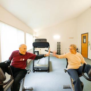 An elderly couple enjoying a workout session on exercise bikes at the gym.