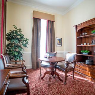 A classic living room with elegant furniture, featuring a round table and chairs, a wooden bookshelf, and a potted plant by the window.