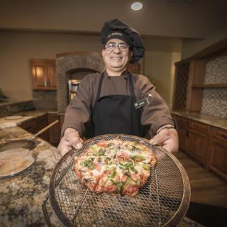 A chef proudly presenting a freshly made pizza in a kitchen setting.