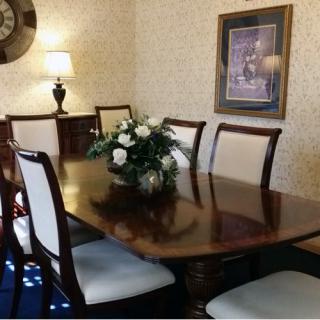 A classic dining room featuring a polished wooden table and chairs, adorned with a flower arrangement.