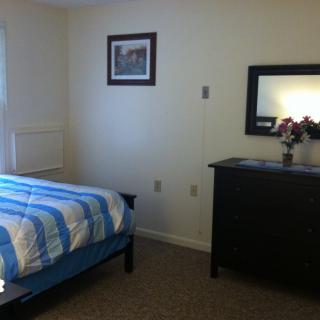 A simple bedroom with a bed, dresser, and wall decorations.