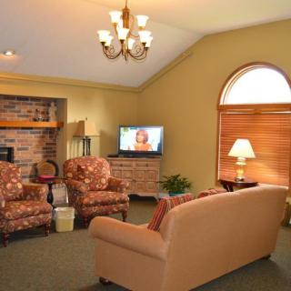 A cozy living room with a sofa, armchairs, and a TV, illuminated by natural light from a large window.