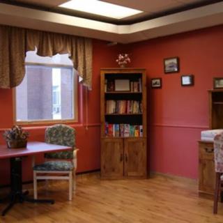 A cozy room with warm-colored walls, featuring a bookshelf filled with books, a window with curtains, and a small table with chairs.