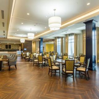 A modern restaurant interior featuring wooden floors, elegant lighting, and neatly arranged tables and chairs.